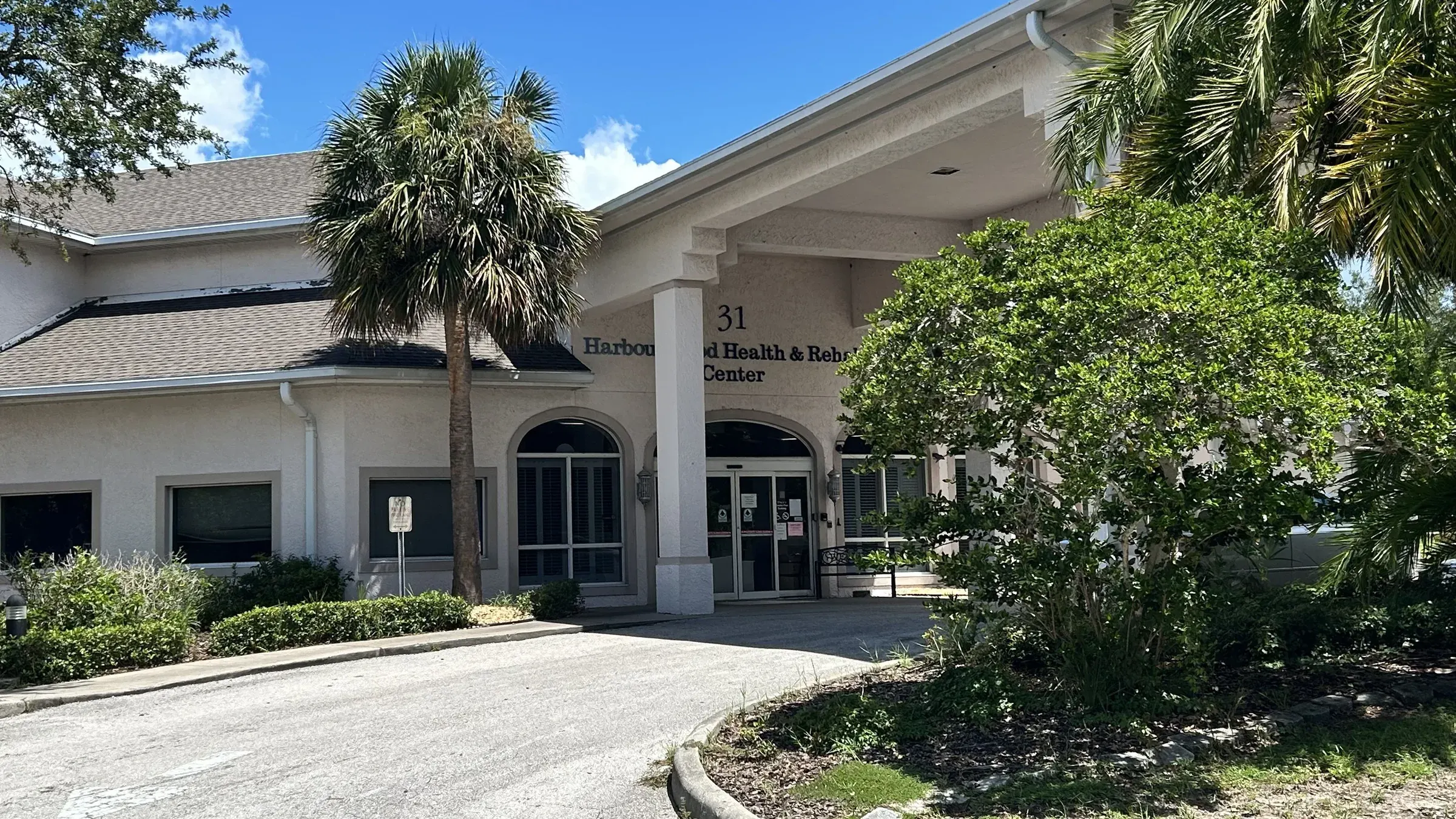 The entrance of Vivo Healthcare Harbourwood, under its palms